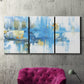 Three-panel canvas wall art featuring blue toned abstract city rhythm, displayed in a living room above a suede accent chair.
