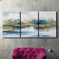 Three-panel canvas wall art featuring abstract blue watercolor landscape, displayed in a living room above a suede accent chair.