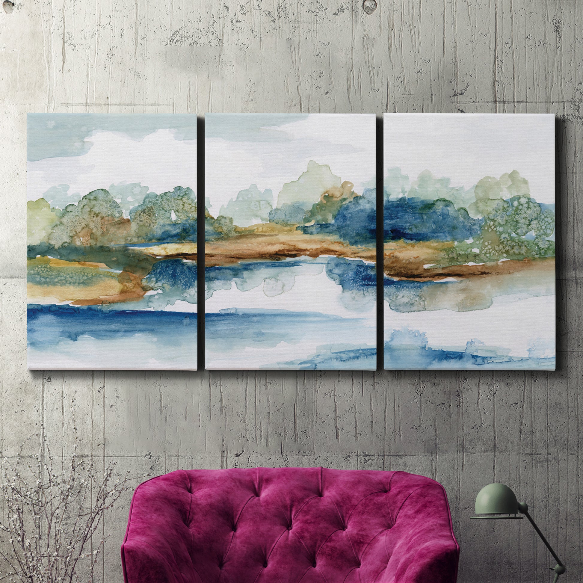 Three-panel canvas wall art featuring abstract blue watercolor landscape, displayed in a living room above a suede accent chair.