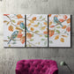 Three-panel canvas wall art featuring decorative bird trio illustration, displayed in a living room above a suede accent chair.
