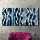 Three-panel canvas wall art featuring flowing blue watercolor wave forms, displayed in a living room above a suede accent chair.