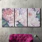 Three-panel canvas wall art featuring soft pink peonies in bloom, displayed in a living room above a suede accent chair.