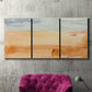 Three-panel canvas wall art featuring minimal horizon with soft blue tones, displayed in a living room above a suede accent chair.