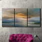 Three-panel canvas wall art featuring tranquil beach at sunset, displayed in a living room above a suede accent chair.