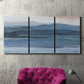 Three-panel canvas wall art featuring wide lake with distant shoreline, displayed in a living room above a suede accent chair.