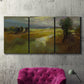 Three-panel canvas wall art featuring winding rural road through countryside, displayed in a living room above a suede accent chair.