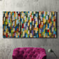 Three-panel canvas wall art featuring colorful confetti style abstraction, displayed in a living room above a suede accent chair.