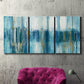 Three-panel canvas wall art featuring layered abstract earth tones, displayed in a living room above a suede accent chair.