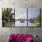 Three-panel canvas wall art featuring river view with boats and reflections, displayed in a living room above a suede accent chair.