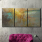 Three-panel canvas wall art featuring muted abstract river inspired tones, displayed in a living room above a suede accent chair.