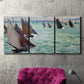 Three-panel canvas wall art featuring sailboat regatta near coastal village, displayed in a living room above a suede accent chair.