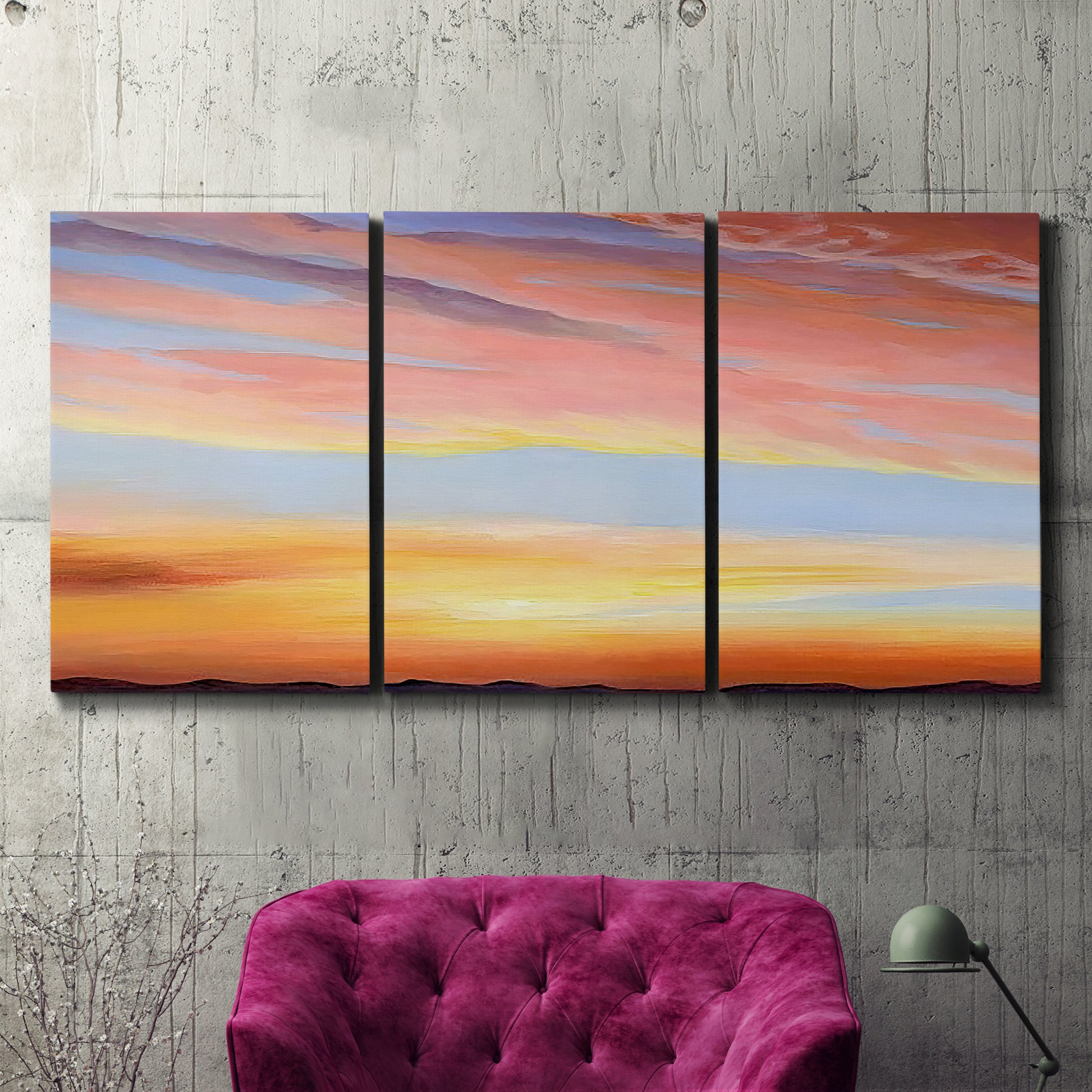 Three-panel canvas wall art featuring glowing sunset sky over landscape, displayed in a living room above a suede accent chair.