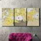 Three-panel canvas wall art featuring abstract floral table arrangement, displayed in a living room above a suede accent chair.