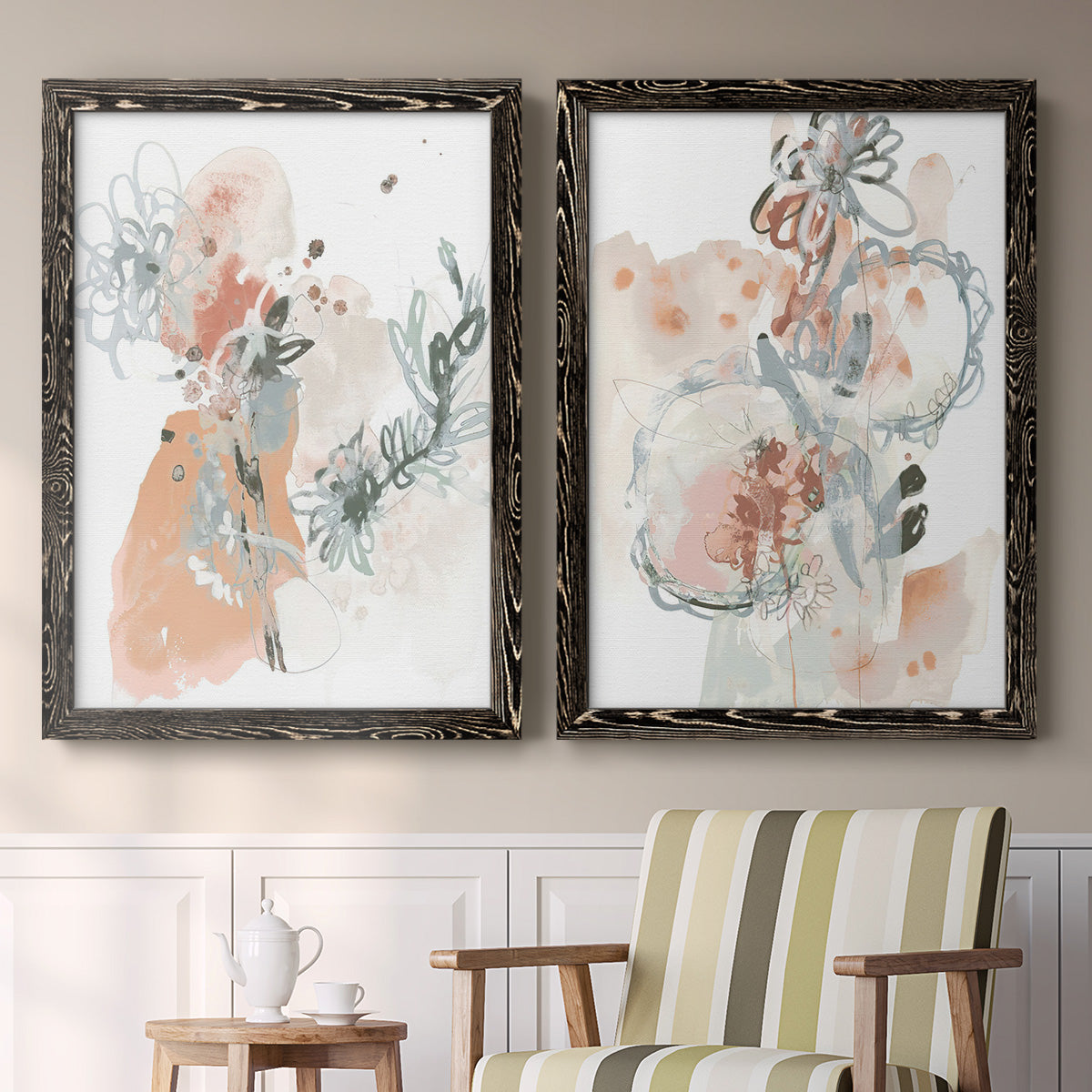 Set of two black barnwood framed canvas prints depicting two abstract watercolor botanicals featuring loose blush gray and coral floral gestures above a sideboard in a cozy sitting room.