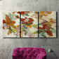 Three-panel canvas wall art featuring layered floral botanical impressions, displayed in a living room above a suede accent chair.