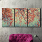 Three-panel canvas wall art featuring autumn foliage landscape photograph, displayed in a living room above a suede accent chair.