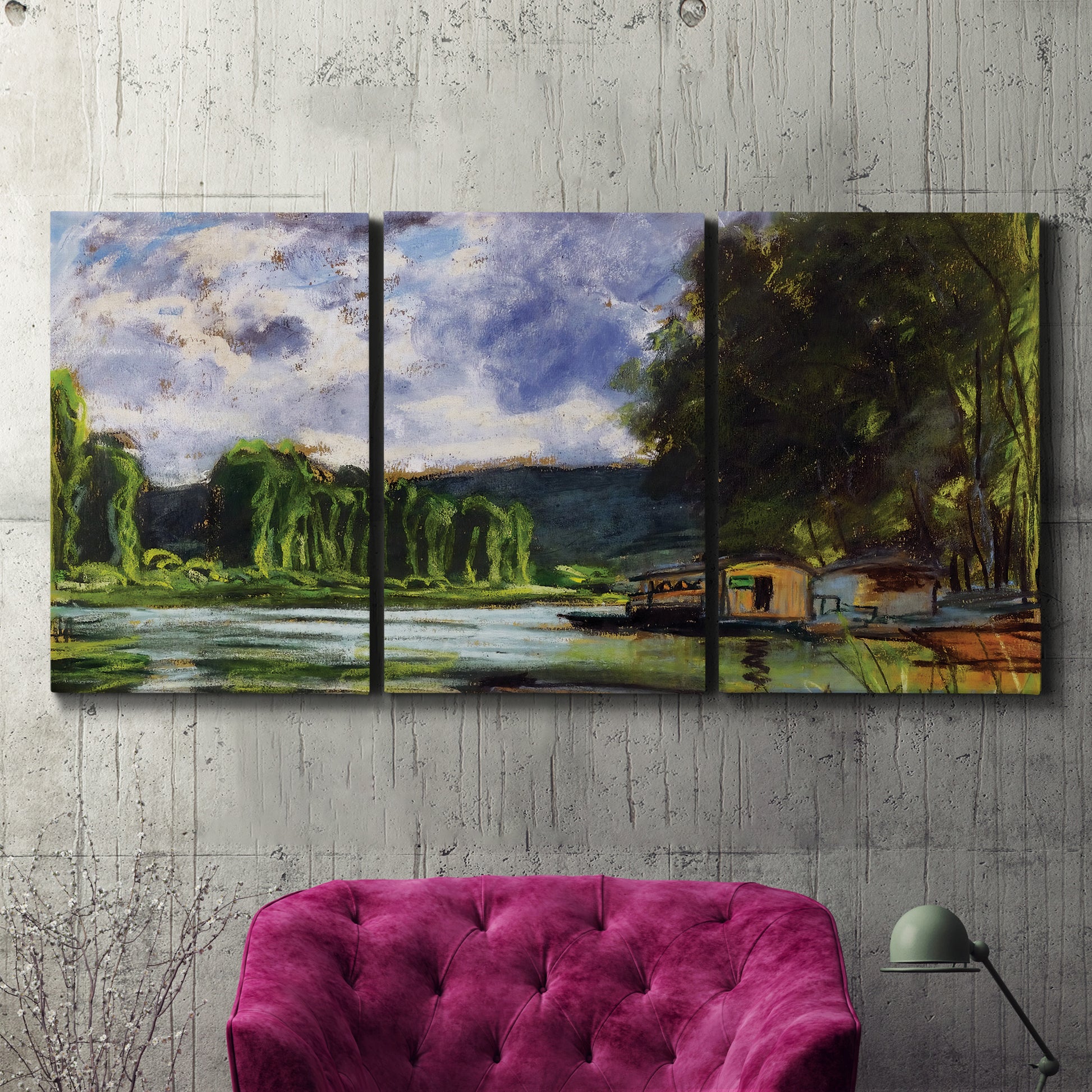 Three-panel canvas wall art featuring riverbank landscape near village, displayed in a living room above a suede accent chair.