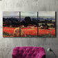 Three-panel canvas wall art featuring red poppy field near barn, displayed in a living room above a suede accent chair.