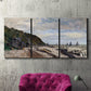 Three-panel canvas wall art featuring open sea along rocky shore, displayed in a living room above a suede accent chair.