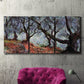 Three-panel canvas wall art featuring pine trees silhouetted at evening, displayed in a living room above a suede accent chair.