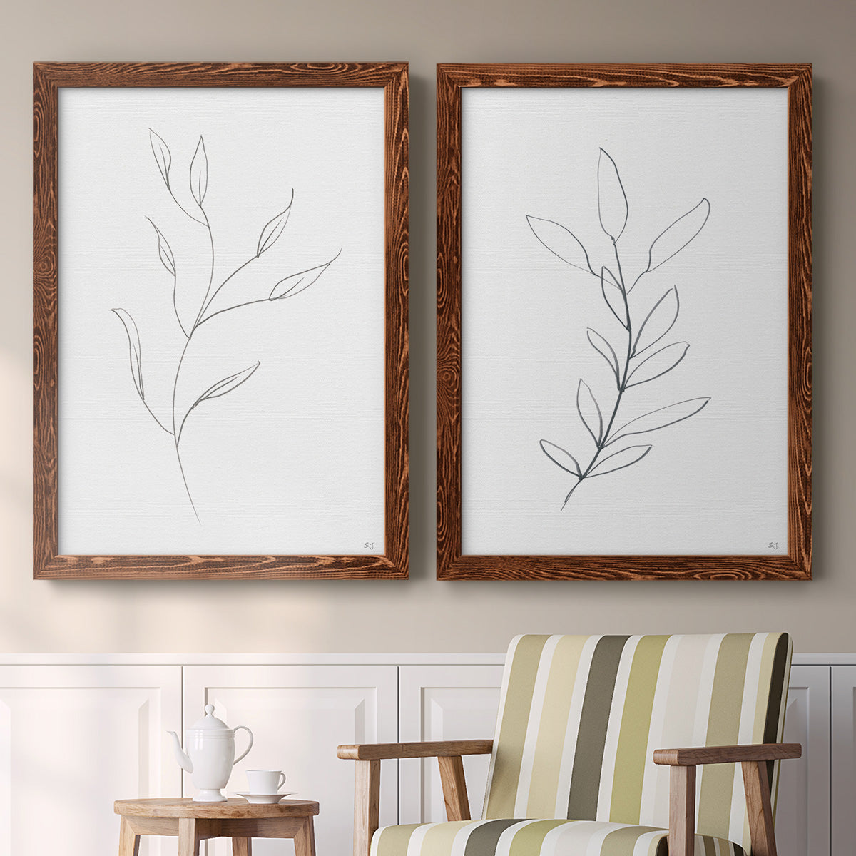 Set of two maple barnwood framed canvas prints depicting two minimalist botanical line drawings featuring single continuous-line leafy branches above a sideboard in a cozy sitting room.