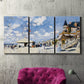 Three-panel canvas wall art featuring beach boardwalk with figures, displayed in a living room above a suede accent chair.