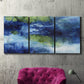 Three-panel canvas wall art featuring flowing blue abstract watercolor, displayed in a living room above a suede accent chair.