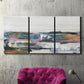 Three-panel canvas wall art featuring cheerful abstract coastal seascape, displayed in a living room above a suede accent chair.