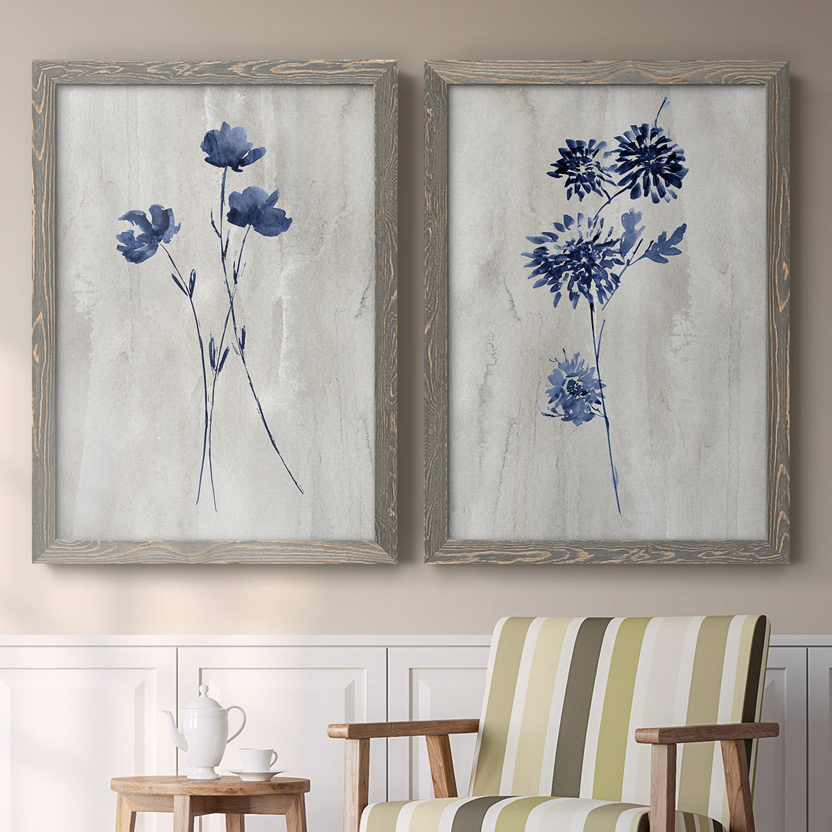 Set of two gray barnwood framed canvas prints depicting two rustic monochrome botanical paintings featuring blue wildflower stems on weathered neutral paper above a sideboard in a cozy sitting room.