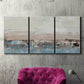 Three-panel canvas wall art featuring abstract bridge landscape in cyan, displayed in a living room above a suede accent chair.