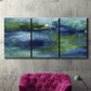 Three-panel canvas wall art featuring flowing blue abstract watercolor, displayed in a living room above a suede accent chair.