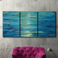 Three-panel canvas wall art featuring deep blue ocean water abstraction, displayed in a living room above a suede accent chair.