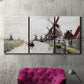 Three-panel canvas wall art featuring windmills beside calm water, displayed in a living room above a suede accent chair.