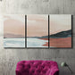 Three-panel canvas wall art featuring quiet coastline with distant horizon, displayed in a living room above a suede accent chair.