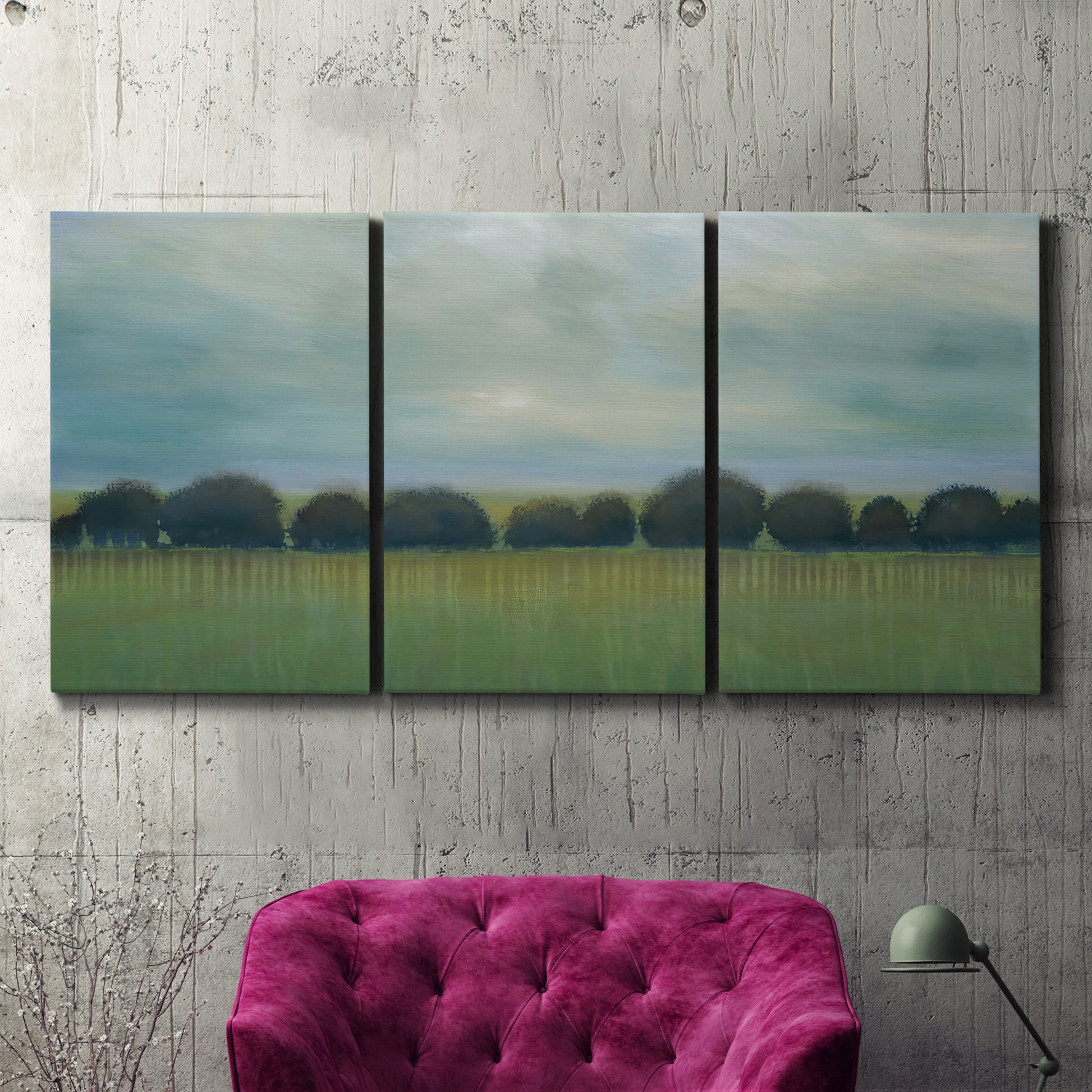 Three-panel canvas wall art featuring rolling green pastoral fields, displayed in a living room above a suede accent chair.