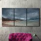 Three-panel canvas wall art featuring stormy sea glass toned coastline, displayed in a living room above a suede accent chair.