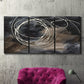 Three-panel canvas wall art featuring dark swirling abstract motion, displayed in a living room above a suede accent chair.