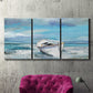 Three-panel canvas wall art featuring classic coastal harbor with boats, displayed in a living room above a suede accent chair.