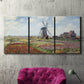 Three-panel canvas wall art featuring tulip fields with windmill, displayed in a living room above a suede accent chair.