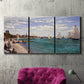 Three-panel canvas wall art featuring river basin with boats, displayed in a living room above a suede accent chair.