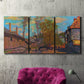 Three-panel canvas wall art featuring wooded stream landscape, displayed in a living room above a suede accent chair.