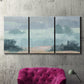 Three-panel canvas wall art featuring soft pastel valley landscape, displayed in a living room above a suede accent chair.