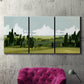 Three-panel canvas wall art featuring lush green summer countryside, displayed in a living room above a suede accent chair.