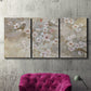 Three-panel canvas wall art featuring early spring blossoms in soft tones, displayed in a living room above a suede accent chair.