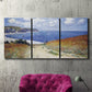 Three-panel canvas wall art featuring coastal path leading to sea, displayed in a living room above a suede accent chair.
