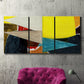 Three-panel canvas wall art featuring geometric mid century abstract blocks, displayed in a living room above a suede accent chair.