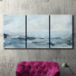 Three-panel canvas wall art featuring abstract sailboats on water, displayed in a living room above a suede accent chair.