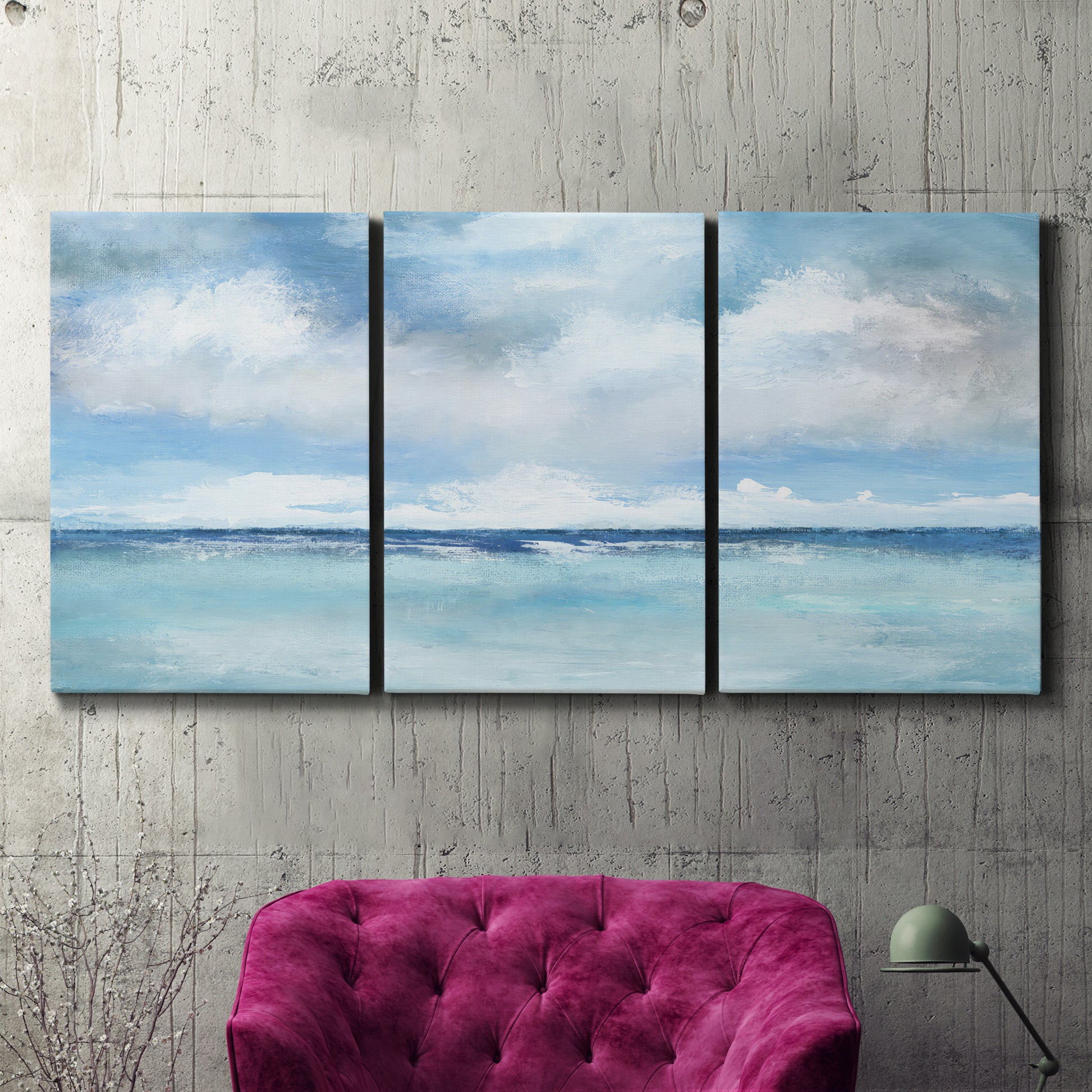 Three-panel canvas wall art featuring tropical clouds over ocean horizon, displayed in a living room above a suede accent chair.