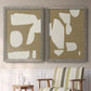 Set of two gray barnwood framed canvas prints depicting two bold minimalist shape abstracts featuring irregular white cutout-like shapes on taupe grounds above a sideboard in a cozy sitting room.