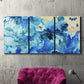 Three-panel canvas wall art featuring abstract coastal beach color fields, displayed in a living room above a suede accent chair.